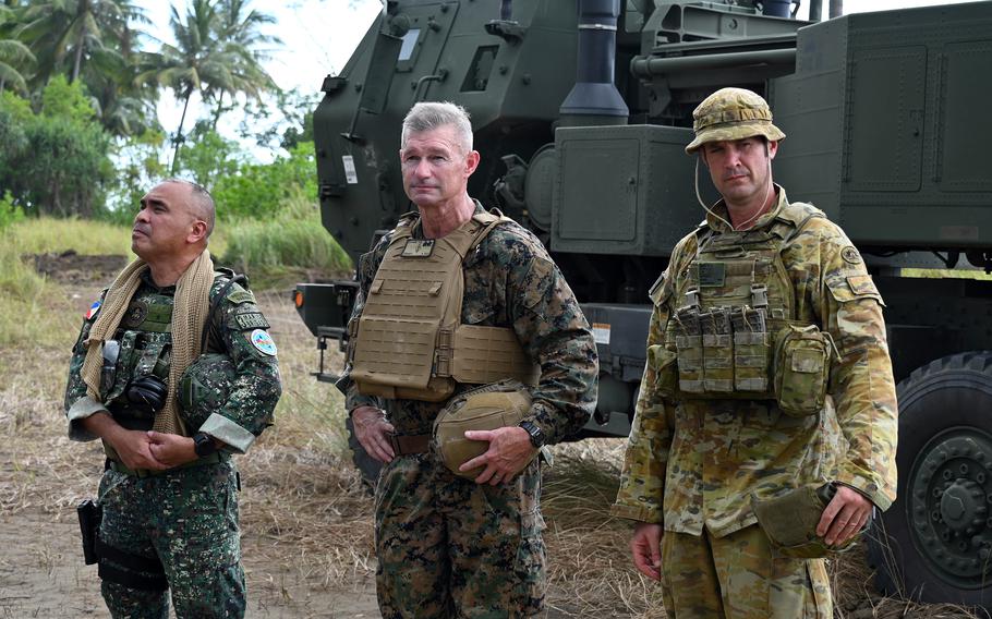 Military leaders wearing bullet-proof vests prepare to address the media in front of a military vehicle.