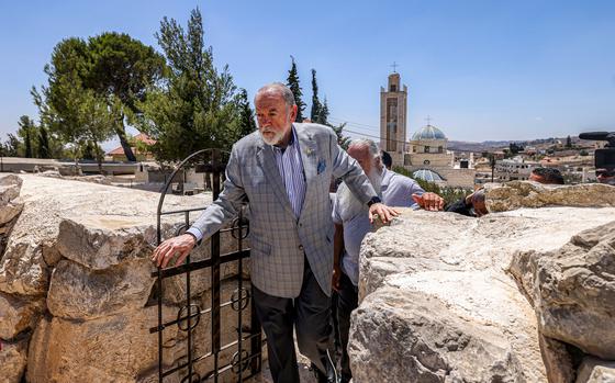 A man walks through the gate of a stone fence.
