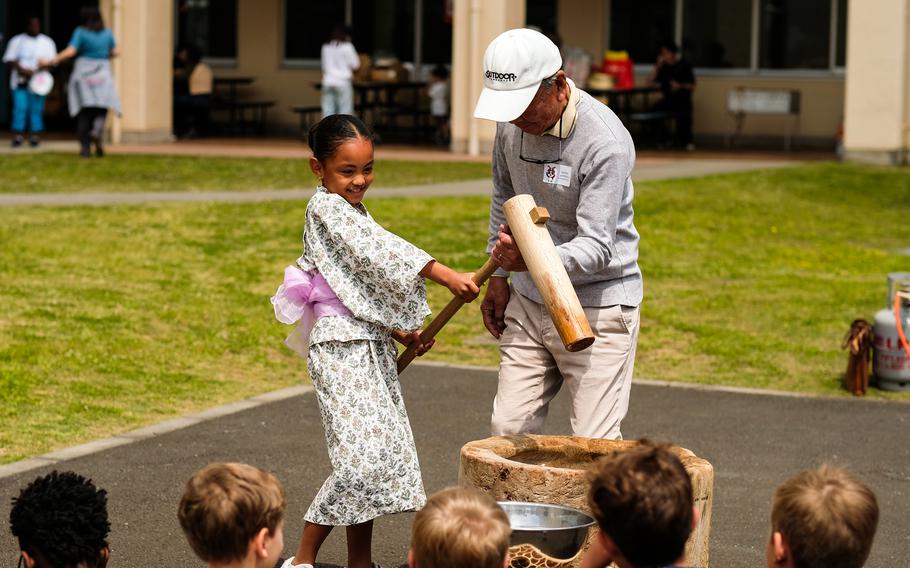 A volunteer helps a Joan K. Mendel Elementary student pound mochi.