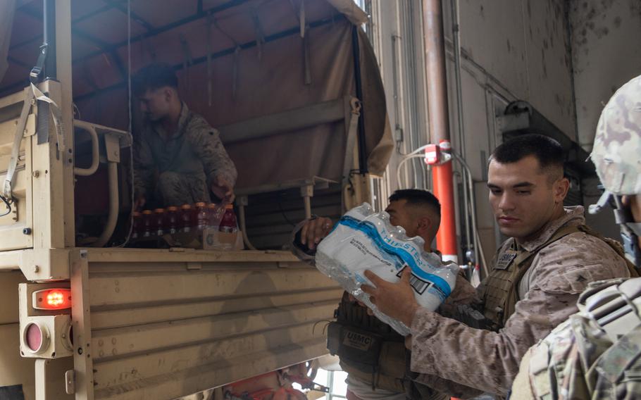 A Marine unloads a case of water from the back of a truck.