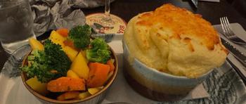 Carrots potatoes and brocolli in a bowl next to a bowl of ground beef and gravy topped with mashed potatoes with melted cheese
