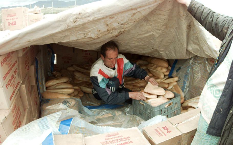 A refugee volunteer gathers bread that was sitting underneath a tarp at the Brazda refugee camp, April 18, 1999.