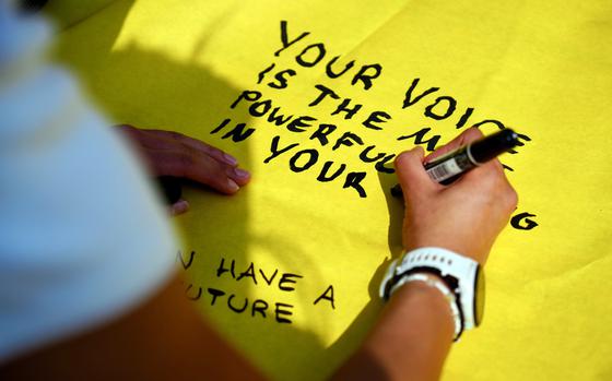 Close-up view of a high school student using a black marker to write a message of protest on a yellow sign.