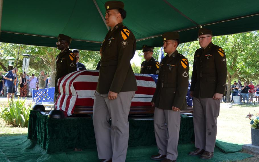 Soldiers stand on both sides of a coffin that has an American flag draped over it.