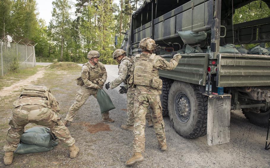 Several soldiers move sandbags into a truck.