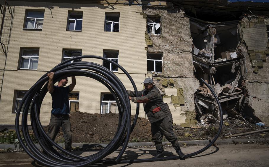 Municipal workers prepare a new tube to restore water supply in front of the building damaged by a Russian attack in Bahmut, Ukraine, on Thursday, May 12, 2022.