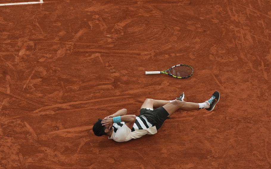 Alcaraz falls backward onto the clay in celebration.