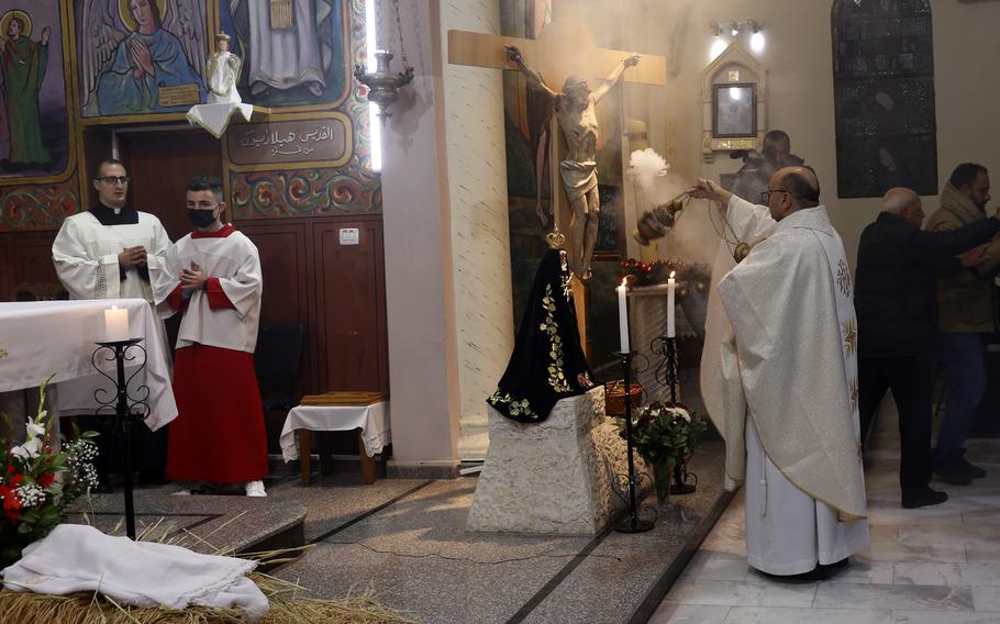 A priest in white robes praying before a crucifix statue.
