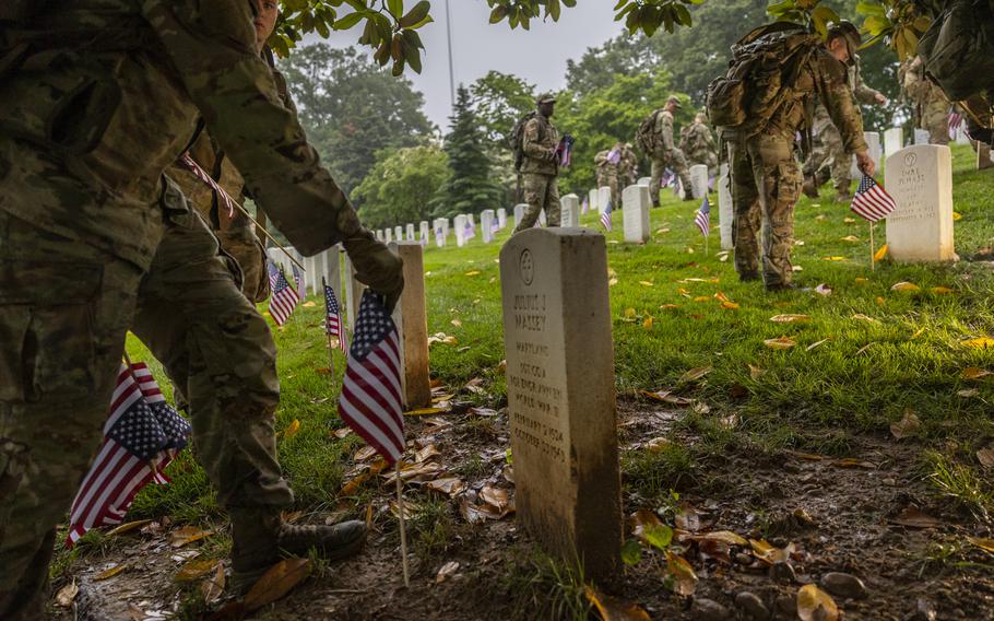 A soldier places a flag in front of a headstone.