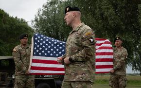 A U.S. soldier speaks in front of an American flag.