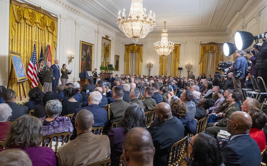 A crowd seated in chairs watches as Joe Biden awards the Medal of honor to a man in a military dress uniform.