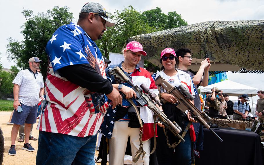 People draped in American flag shirts and jackets hold rifles.