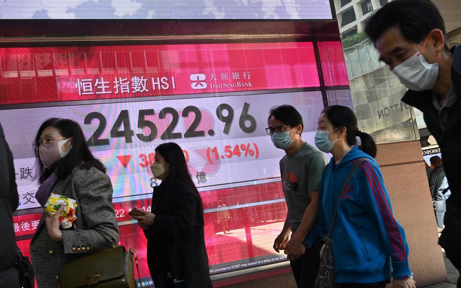 People walk past a sign showing the numbers for the Hang Seng Index before it closes, as Hong Kong shares fell by the most in two weeks, on Monday, Feb. 14, 2022 as the fifth wave of COVID-19 infections in the city worsened. 
