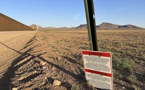 A warning sign mounted on a green metal post stands in an arid desert landscape with brown, rocky terrain.