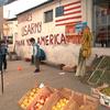 Children play soccer next to outdoor produce stands and in front of a wall with “Thank you America” painted on it.