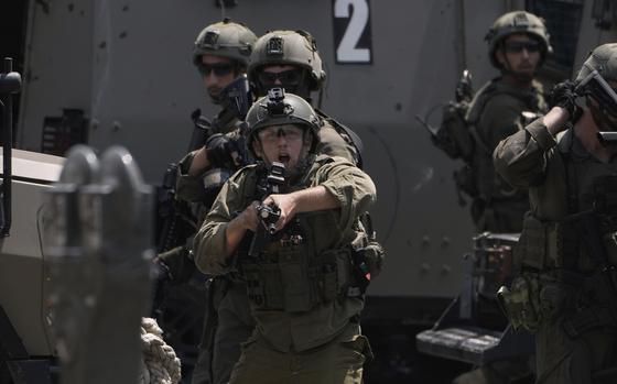 A soldier in green combat gear points a weapon forward as other soldiers watch from behind.