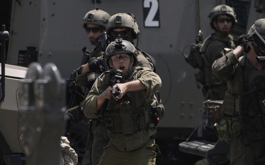 A soldier in green combat gear points a weapon forward as other soldiers watch from behind.