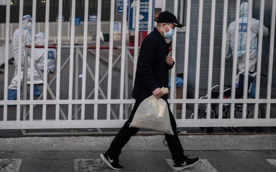 A man carries a bag as he walks by epidemic control workers wearing PPE to protect against the spread of COVID-19 as he leaves after being released from a government quarantine facility on Dec., 7, 2022 in Beijing. As part of a 10 point directive, China's government announced Wednesday that people with COVID-19 who have mild or are asymptomatic will be permitted to quarantine at home instead of being taken to a makeshift facility, a major shift in its zero COVID policy.  (Kevin Frayer/Getty Images/TNS)