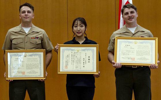 Marine Corps Sgt. William Carroll, left, restaurant worker Ami Amemiya, center, and Sgt. Jarrett Fuqua pose with letters of appreciation from the city of Gotemba, Japan, June 21, 2023. The trio worked together to save a choking man's life a month earlier.