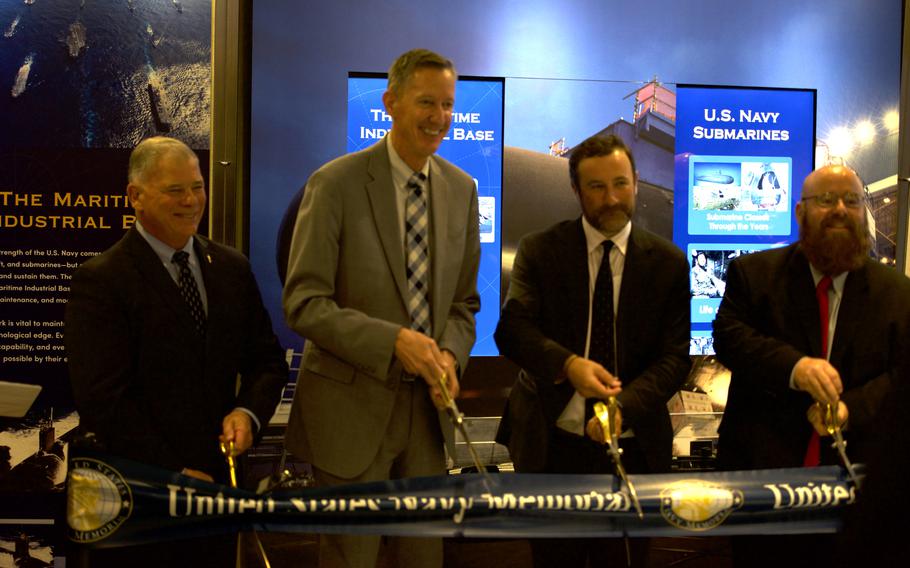 Four men in suits and ties hold large scissors over a ribbon they are about to cut.