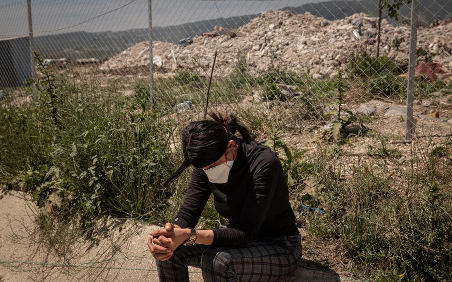 A woman sits in front of a rubble dump site in Samandag.