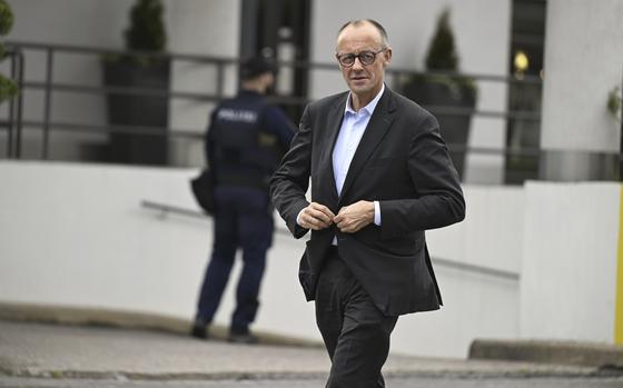 Friedrich Merz buttons his jacket and walks in the street.