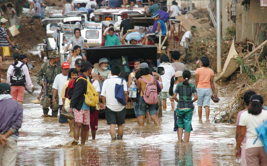 People walk through muddy water in the town Infanta beside a distribution point for U.S. Marines delivering aid as part of a Joint Task Force humanitarian mission to the Philippines.