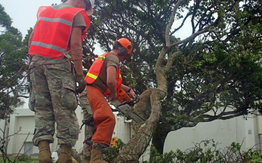 Airman 1st Class Joseph Green, 21, left, from Springfield, Mass., and Staff Sgt Skyler Cunningham, 26, from Knoxville, Iowa, of the 18th Civil Engineering Squadron, Kadena Air Base, Okinawa, Japan, discard branches at Kadena High School, Aug. 7, 2023.