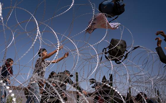 Migrants from Colombia and Mexico throw their bags over razor wire fencing after crawling through an opening in the border wall between El Paso, and Juárez, Mexico. MUST CREDIT: Danielle Villasana for The Washington Post.