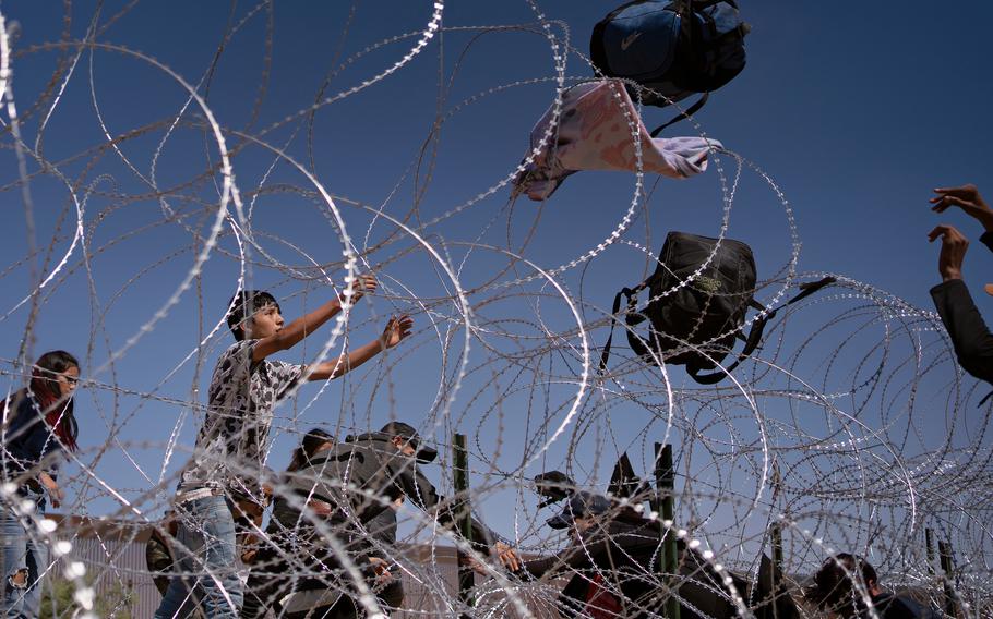 Migrants from Colombia and Mexico throw their bags over razor wire fencing after crawling through an opening in the border wall between El Paso, Texas, and Juárez, Mexico. 