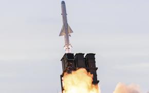A missile emerging from a rocket launcher against a gray sky.