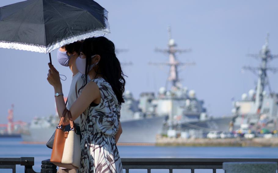 A couple strolls past ships moored at Yokosuka Naval Base, Japan, Friday, Sept. 24, 2021. 