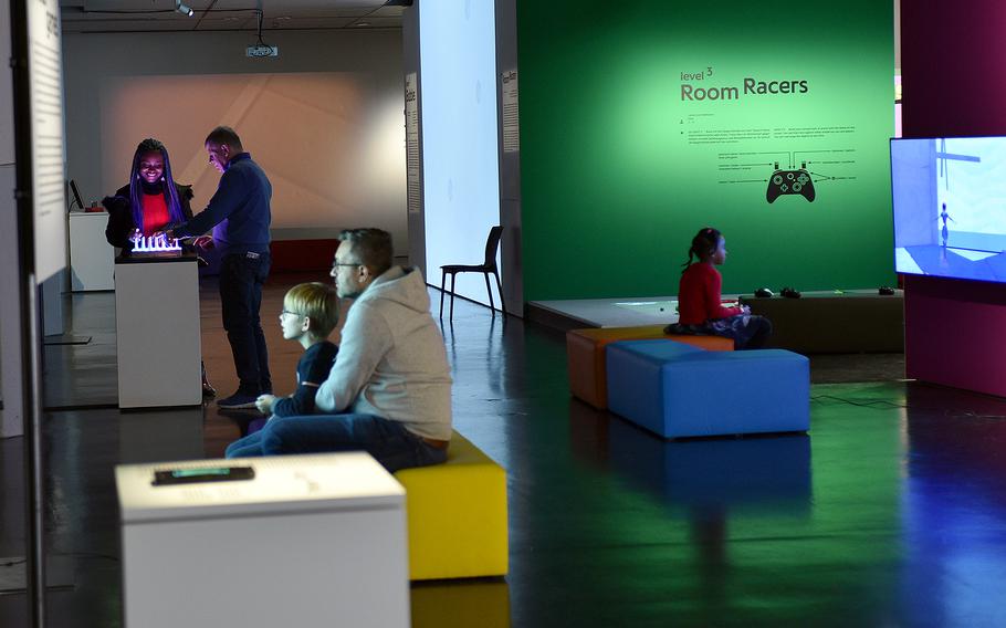 Visitors play games in the “zkm_gameplay. the next level” exhibit at the Zentrum fuer Kunst und Medien Karlsruhe on Nov. 26, 2022, in Karlsruhe, Germany. Featured here are No Man’s Sky, bottom left, a PlayStation 4 game released in 2016; Wobble Garden, top left, a 2017 game that consists of springs with LED lights; and Bound, right, a 2017 PlayStation 4 game that puts players in the mind of a pregnant woman where the main character is a dancing princess.