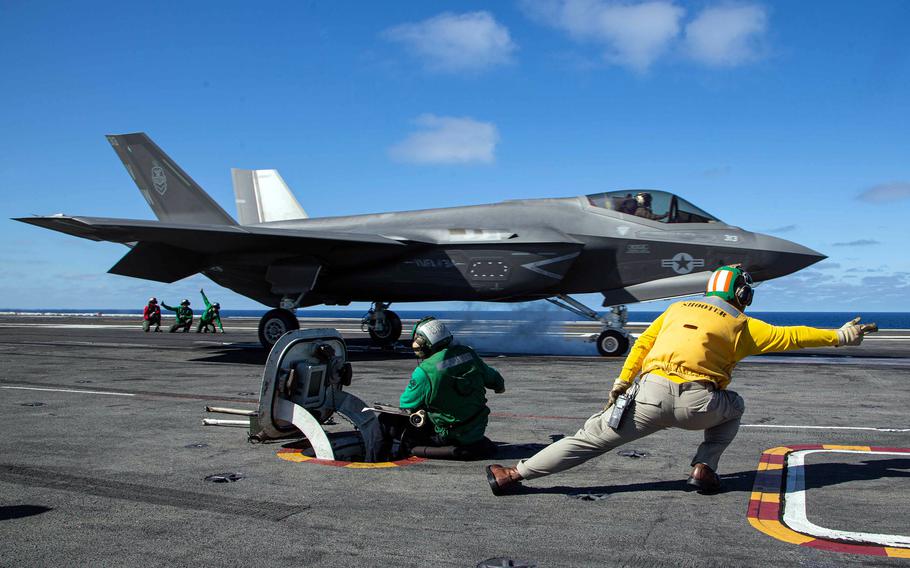 A flight crew directs a military fighter jet as it prepares to take off from the deck of an aircraft carrier.
