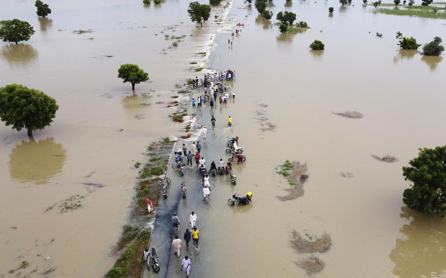 People walk through floodwaters after heavy rainfall in Hadeja, Nigeria, Sept 19, 2022. Publication of a major new United Nations report on climate change is being held up by a battle between rich and developing countries over emissions targets and financial aid to vulnerable nations.