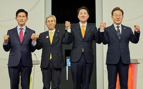 Four men in suits link and hold up their hands while standing on a stage. 