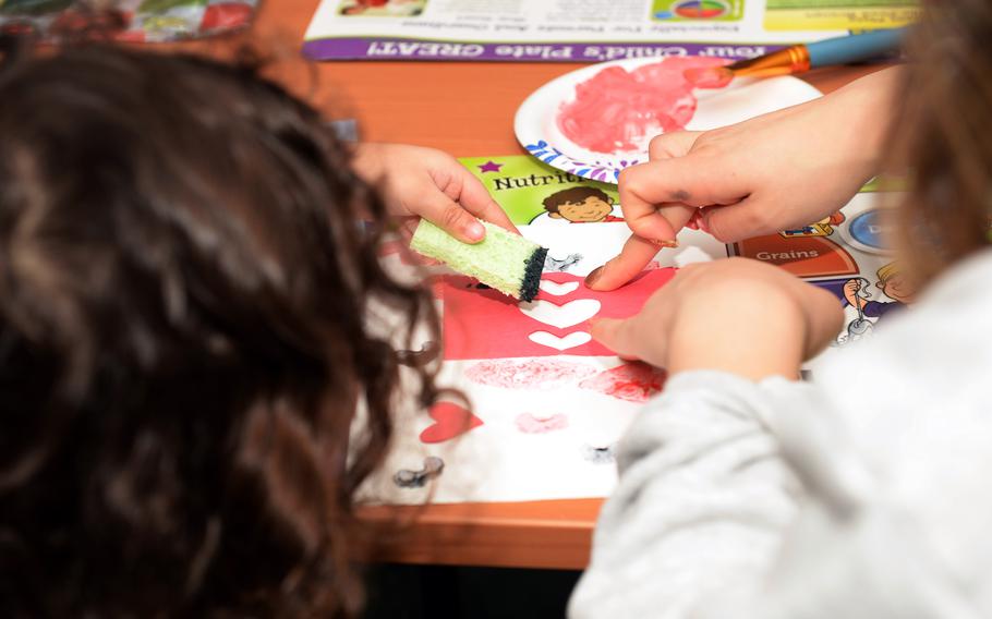 A mother helps her child sponge paint on heart-shaped paper at RAF Lakenheath, England in February 2018, at an event hosted by the Women, Infants and Children Overseas program. Because many military spouses cannot get a job overseas, thousands turn to the WIC Overseas program to buy groceries.