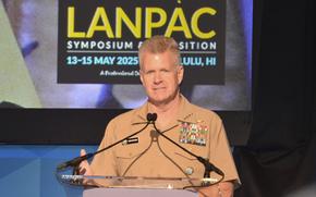 Adm. Samuel Papro in uniform delivers a speech in front of a microphone.
