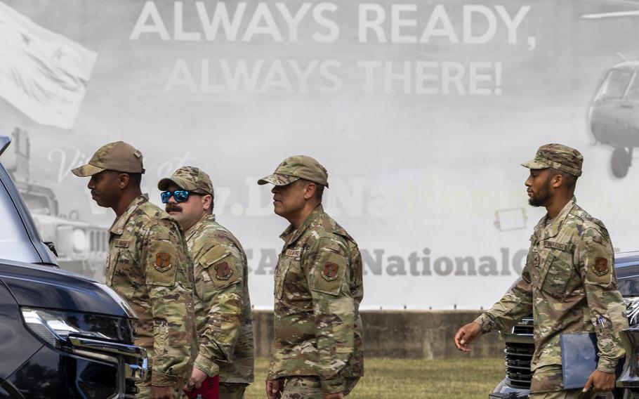 Troops in uniform walk in front of a sign that reads “Always Ready Always There!”