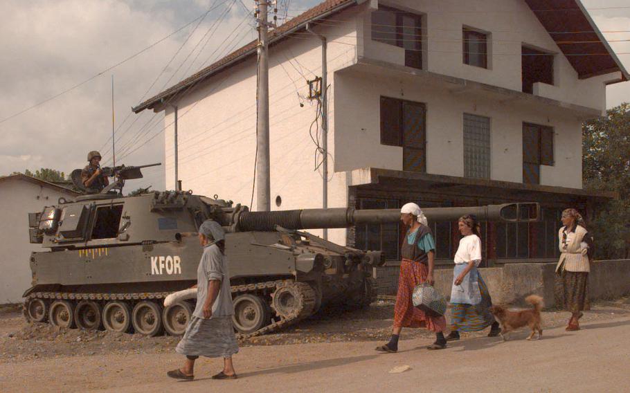 Women walk by an artillery piece.