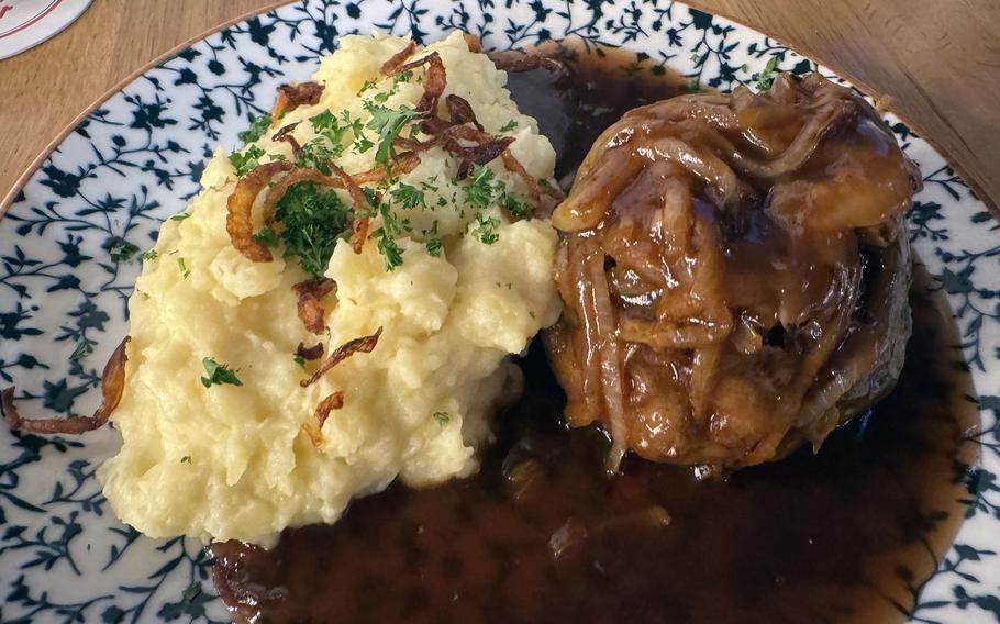 A veal patty in brown gravy next to mashed potatoes on a plate.