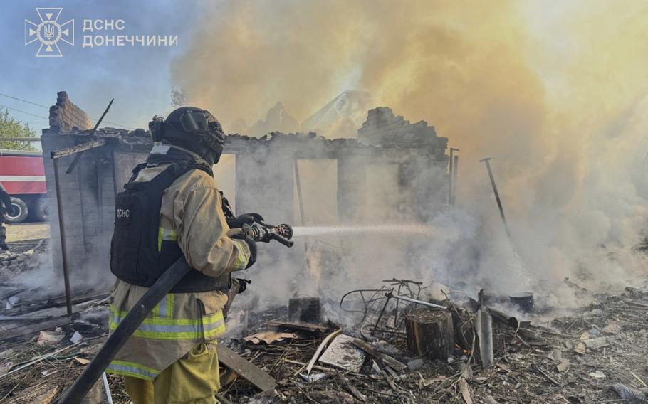A firefighter aims a hose into a destroyed building that is smoking from a recent fire.