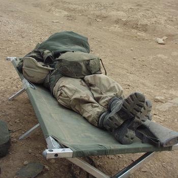 A soldier lies on a cot in the desert.