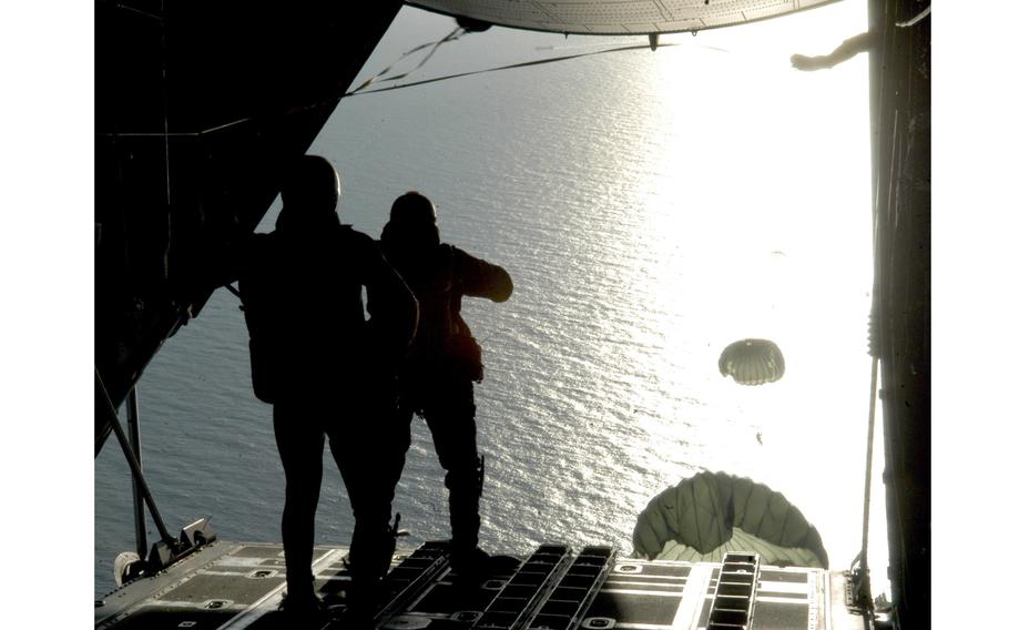 Two service members prepare to jump from the back of an aircraft over the sea