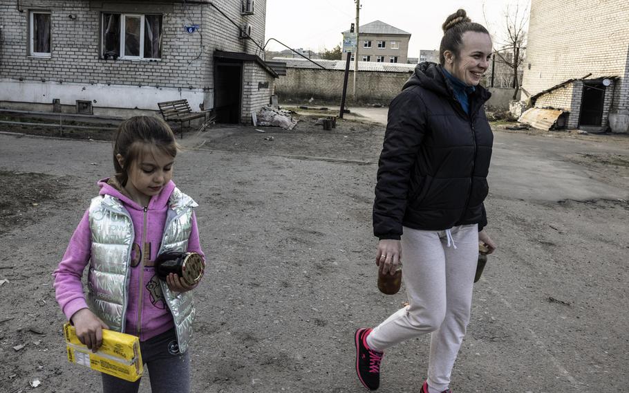 Anastasiya, 7, and her mother, Iryna, carry jars of jam and pickles they received from the distribution of food aid.
