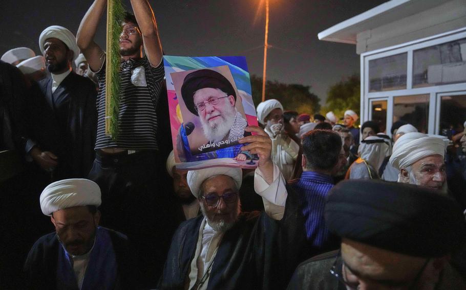 Men protest outside, with one holding a poster of Iran’s supreme leader.
