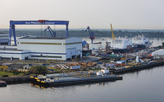 A shipyard by a river with a treeline in the background.
