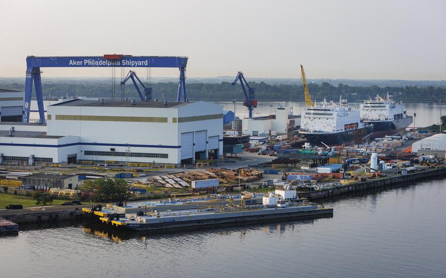A shipyard by a river with a treeline in the background.