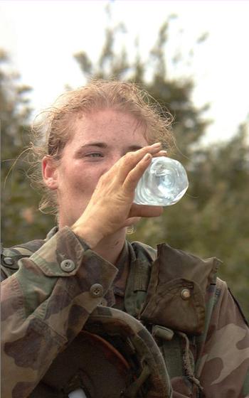 A vertical photo of a soldier drinking from a bottle of water.