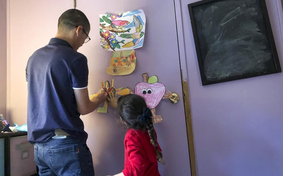 Mohammed Naiem Asadi helps his daughter Zainab, 5, hang up her art at their home in the suburbs of Atlantic City, N.J., Oct. 26, 2021.